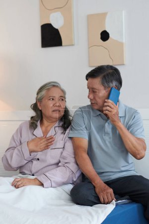 Foto de Mujer mayor quejándose de dolor de corazón y marido llamando al médico - Imagen libre de derechos