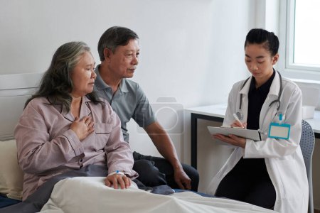 Téléchargez les photos : Médecin généraliste prenant des notes lors de la conversation avec une femme âgée malade et son mari - en image libre de droit