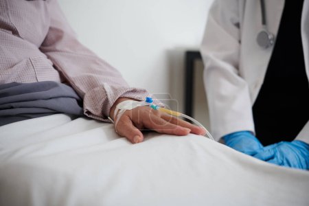 Foto de Mujer mayor enferma sentada en la cama con catéter en la mano - Imagen libre de derechos