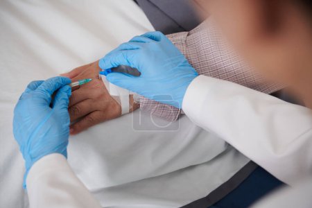 Foto de Imagen de primer plano del médico insertando catéter intravenoso en la mano del paciente - Imagen libre de derechos