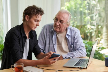 Photo for Senior man listening to grandson explaining how to use application on smartphone - Royalty Free Image