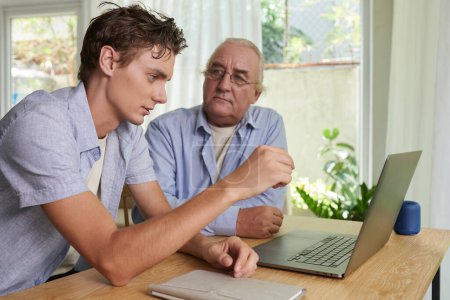 Photo for Serious young man explaining grandfather how to send e-mails and make video calls - Royalty Free Image