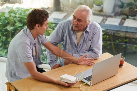Photo for Young man explaining grandfather how wi-fi works - Royalty Free Image