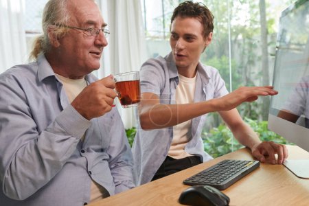Photo for Cheerful young man showing grandfather how to buy plain ticket online - Royalty Free Image