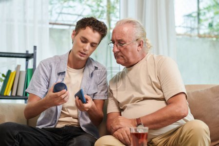Téléchargez les photos : Jeune homme expliquant grand-père comment connecter smartphone avec haut-parleur - en image libre de droit