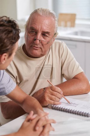 Téléchargez les photos : Homme âgé discutant du budget familial avec son fils adulte, lui apprenant à calculer ses dépenses - en image libre de droit