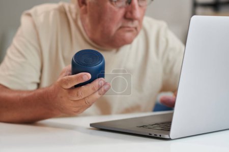 Photo for Senior man connecting speaker to laptop to listen to music from playlist - Royalty Free Image