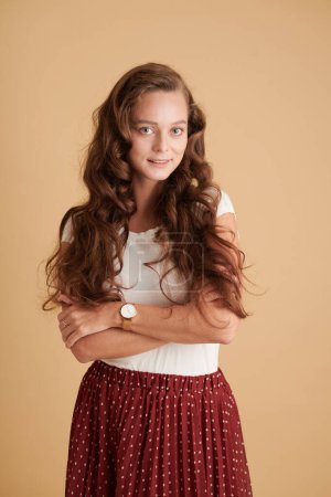 Téléchargez les photos : Portrait studio de fille souriante aux cheveux bouclés marron clair croisant les bras et regardant la caméra - en image libre de droit