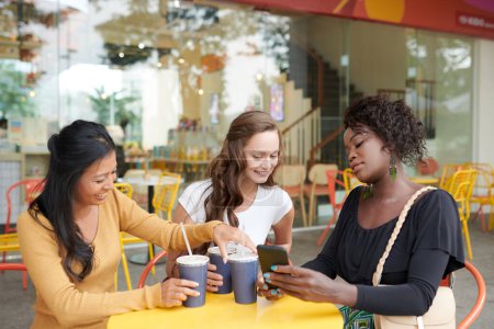 Foto de Mujer joven mostrando fotos en el teléfono inteligente a los amigos cuando están tomando refrescos en la mesa de café - Imagen libre de derechos