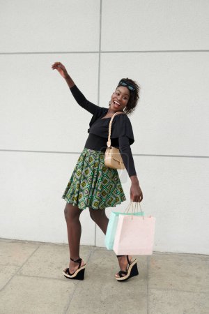Foto de Emocionado joven mujer negra disfrutando bailando al aire libre con bolsas de compras - Imagen libre de derechos
