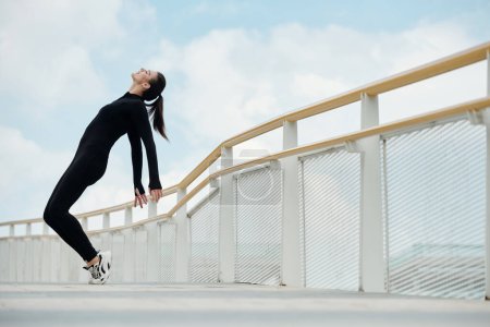 Photo for Happy female dancer in black jumpsuit doing toe stand on bridge - Royalty Free Image