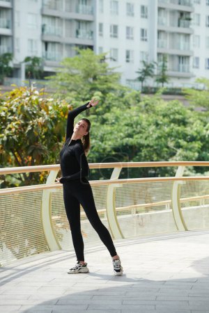 Téléchargez les photos : Jeune femme en unitard noir profitant de la danse en plein air sur une journée ensoleillée - en image libre de droit