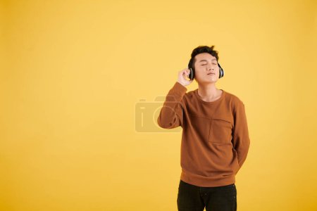 Photo for Vietnamese young man in headphones closing eyes when listening to his favorite music - Royalty Free Image
