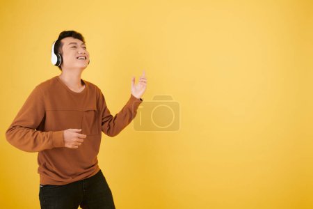 Foto de Feliz joven asiático bailando con música en auriculares y tocando guitarra invisible - Imagen libre de derechos