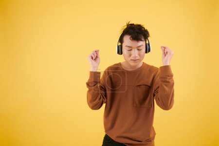 Photo for Young man closing eyes and snapping fingers to follow rhythm of song playing in headphones - Royalty Free Image