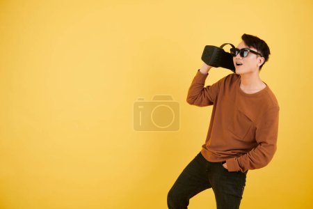 Téléchargez les photos : Joyeux jeune homme dans les lunettes de soleil portant haut-parleur avec jouer de la musique - en image libre de droit