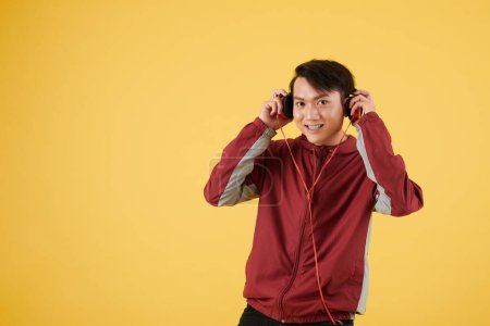 Foto de Sonriente joven deportista asiático en chaqueta roja con auriculares para correr o hacer ejercicio con música - Imagen libre de derechos
