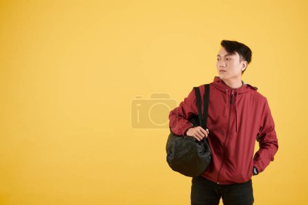 Téléchargez les photos : Portrait d'un jeune sportif souriant tenant un sac de sport avec des baskets et des vêtements de sport - en image libre de droit