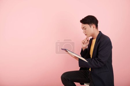 Téléchargez les photos : Pensive jeune entrepreneur asiatique lecture rapport ou accord sur tablette informatique - en image libre de droit