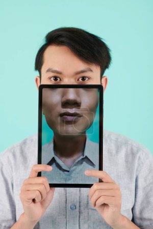 Téléchargez les photos : Jeune homme asiatique tenant tablette avec son portrait à l'écran - en image libre de droit