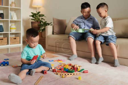 Photo for Two preteen boys playing ukulele when their younger brother playing with toy bricks on the floor - Royalty Free Image