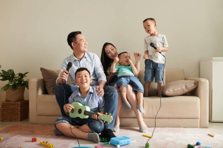 Foto de Feliz familia asiática de cinco riéndose, tocando ukelele y cantando canción en el micrófono - Imagen libre de derechos