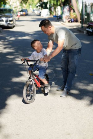 Photo for Happy father teaching little son how to ride bicycle on sunny summer day - Royalty Free Image
