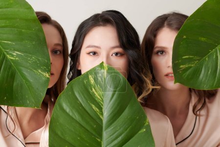 Téléchargez les photos : Groupe de dispositif grave jeunes femmes couvrant les visages avec des feuilles vertes - en image libre de droit