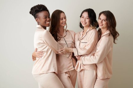 Téléchargez les photos : Groupe diversifié d'amies en pyjama de soie qui se sourient et se serrent dans leurs bras - en image libre de droit