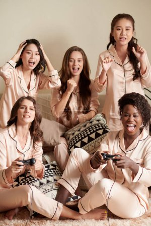 Foto de Grupo de amigos emocionales apoyando a dos niñas que juegan videojuegos en casa - Imagen libre de derechos