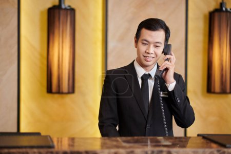 Téléchargez les photos : Réceptionniste vietnamienne souriante en costume élégant faisant un appel téléphonique - en image libre de droit