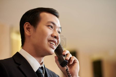 Photo for Smiling Vietnamese hotel receptionist talking on phone - Royalty Free Image