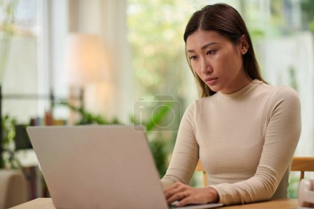 Photo for Serious young woman in beige turtleneck working on laptop at home - Royalty Free Image