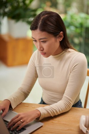 Photo for Pensive young Asian solopreneur working on laptop, programming or answering e-mails - Royalty Free Image