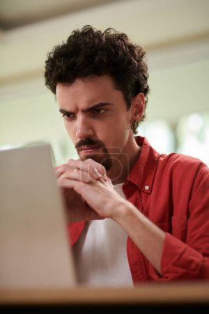 Photo for Frowning man looking at laptop screen with programming code - Royalty Free Image