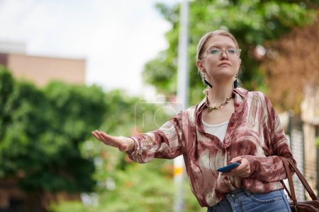 Photo for Serious young woman with smartphone catching taxi - Royalty Free Image