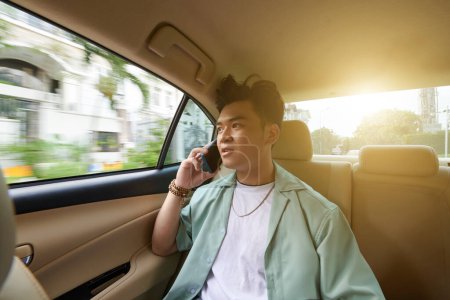 Photo for Young Vietnamese man talking on phone when riding taxi car to work - Royalty Free Image