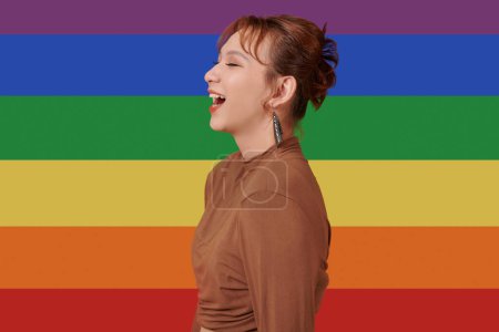 Téléchargez les photos : Portrait de femme transgenre riante debout contre le drapeau arc-en-ciel - en image libre de droit