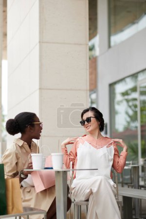 Téléchargez les photos : Jeune femme élégante assise à la table du coffeeshop et discutant des achats - en image libre de droit