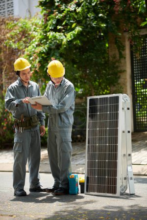 Photo for Contractores in grey uniform reading specifications before installing solar panel - Royalty Free Image