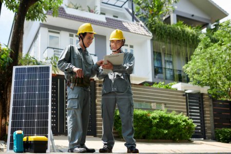 Photo for Solar panel installers checking document with specifications before starting work - Royalty Free Image