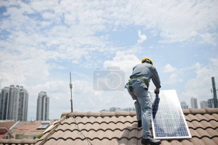 Photo for Worker in hardhat and grey uniform installing solar panel on roof - Royalty Free Image