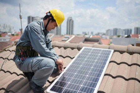 Foto de Trabajador en uniforme y hardhat atornillado panel solar en el techo - Imagen libre de derechos
