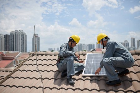 Photo for Team of workers installing solar panels on roof, big city in background - Royalty Free Image
