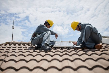 Photo for Contractors in hardhats installing solar panels on roof - Royalty Free Image