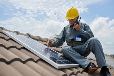Photo for Contractor installing solar panel and using with walkie-talking - Royalty Free Image