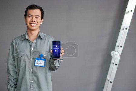 Téléchargez les photos : Portrait de travailleur de service à domicile joyeux montrant smartphone avec application mobile - en image libre de droit