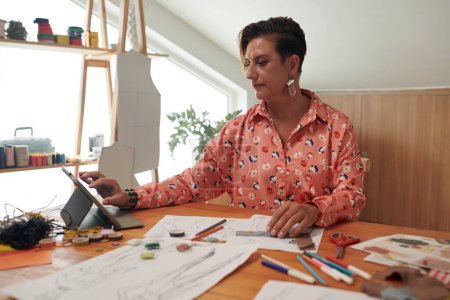 Téléchargez les photos : Portrait de styliste travaillant avec des croquis au bureau dans son atelier - en image libre de droit