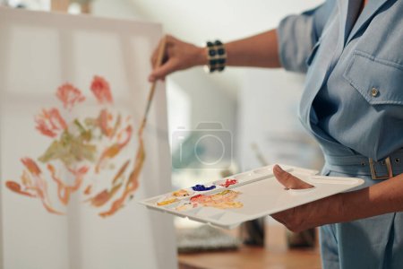 Photo for Artist using plastic palette when painting flowers on canvas - Royalty Free Image