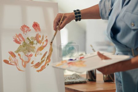 Téléchargez les photos : Image recadrée de femme peignant des fleurs sur toile dans son studio à la maison - en image libre de droit